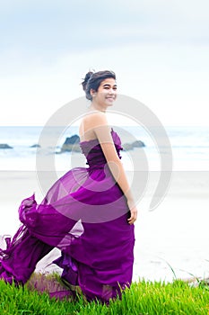 Teen girl wearing purple gown on grassy knoll overlooking ocean photo
