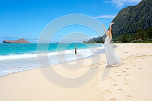 Teen girl in white dress on Hawaiian beack, arms raised