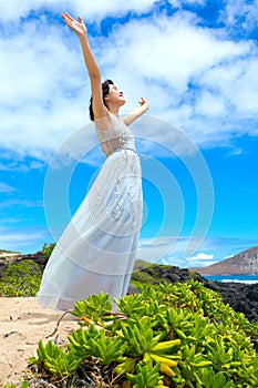 Teen girl in white dress raising arms in praise outdoors