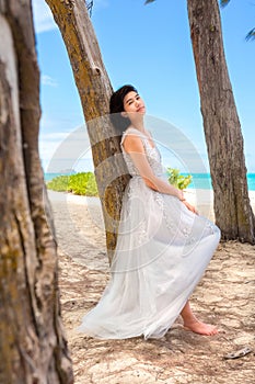 Teen girl in white dress by tree along Hawaiian beach