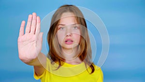 Teen girl in a yellow t-shirt is looks at camera, holds out her hand in a front and says stop