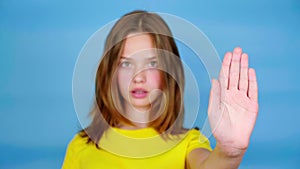 Teen girl in a yellow t-shirt is looks at camera, holds out her hand in a front and says stop