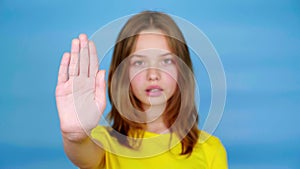 Teen girl in a yellow t-shirt is looks at camera, holds out her hand in a front and says stop