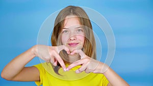 Teen girl in a yellow t-shirt showing heart shape, smiles and looking at camera