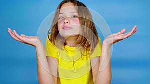 Teen girl in a yellow t-shirt is shrugs and looking at camera, doesn't know