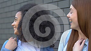 Teen girls gossiping laughing at classmate outdoors, secretly rumor-mongering