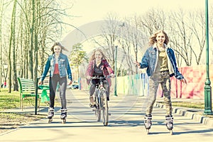 Teen girls roller skating and riding a bicycle at park