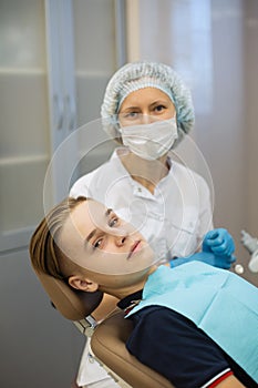 Teen guy patient sitting in a chair and woman dentist