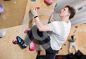 Teen guy practicing rock climbing on climbing wall