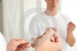 Teen guy using acne healing patch near mirror, focus on hands