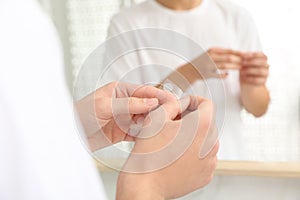 Teen guy using acne healing patch near mirror, focus on hands photo