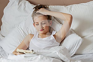 Teen handsome blonde boy lying in white bed  and reading book. Relax time