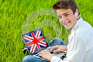 Teen learning english on laptop outdoors.
