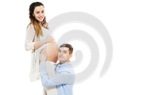 Teen Man Is Listening To His Beautiful Pregnant Wife`s Tummy And Smiling Isolated On White Background photo