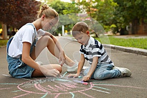 Teen nanny and cute little boy drawing sun with chalks