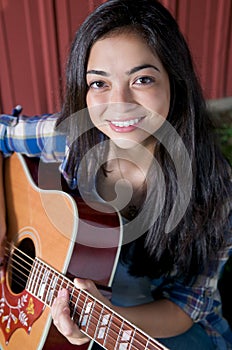 Teen playing guitar by barn