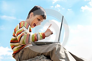 Teen pointing up while playing a laptop outside