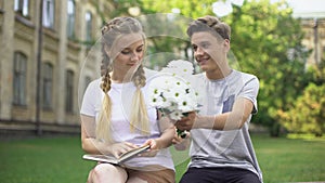 Teen reading book when young man presenting field flowers, first love, flirt