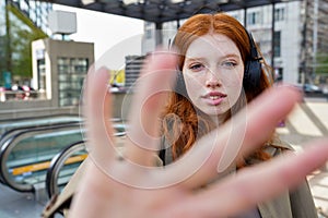 Teen redhead girl wearing headphones looking at camera on city street.