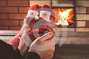 Teen`s hands hold a red cup of coffee in front of the fireplace. Christmas holiday.