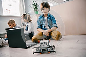 teen schoolboy with laptop and robot sitting on floor