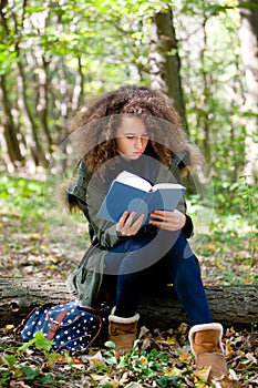 Teen schoolgirl reading book in the autumn park