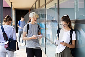 Teen schoolgirl standing with workbook near college building