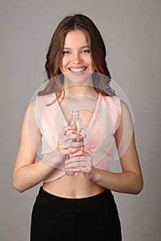 Teen in shirt posing with bottle of water. Close up. Gray background