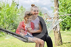 Teen sister girls and child having fun on hammock in the backyard garden