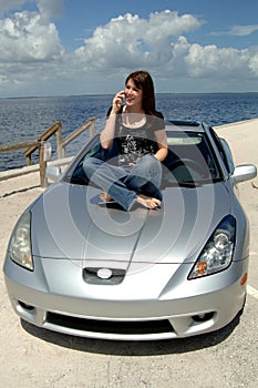 Teen sitting on car hood on cell phone