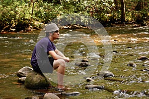 Teen sitting on river rocks, side view