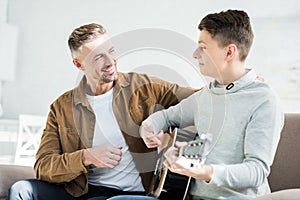 Teen son playing acoustic guitar for cheerful father photo