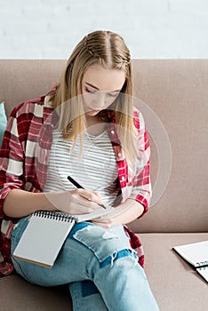 teen student girl writing in notebook while sitting on sofa