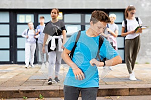 Teen student looking at his watch on way to college