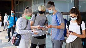 Teen students in medical masks standing with workbooks in schoolyard