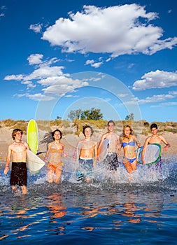 Teen surfers group running beach splashing