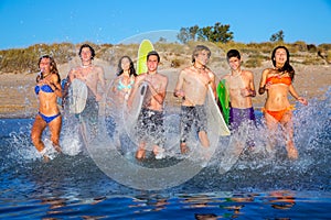 Teen surfers group running beach splashing