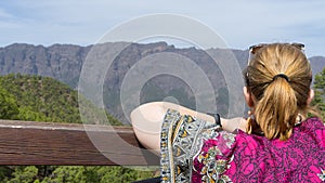 Teen tourist resting, hold a wood fence, relaxing and look the environment national park with colorful dress. Blonde woman observe