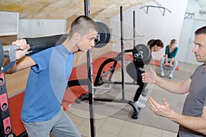 Teen training with weights at gym club with coach