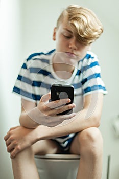 Teen using smartphone on toilet