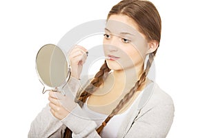 Teen woman applying lipstick looking at mirror.