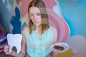 Teen woman holding big white teeth made from paper and plate with sweet