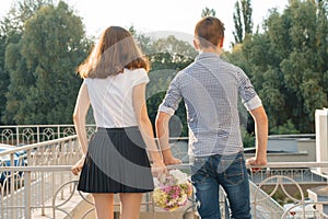 Teen youth couple boy and girl standing back, summer sunny day, girl holding bouquet of flowers in hand