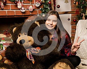 Teenag girl is embraces a big big teddy bear on christmas near fireplace