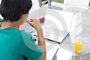 Teenage Asian boy sitting outside at home, focusing on laptop screen, copy space