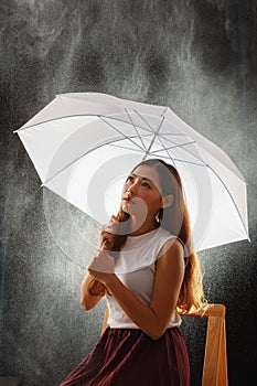 Teenage Asian girl holding umbrella and sitting while rainy