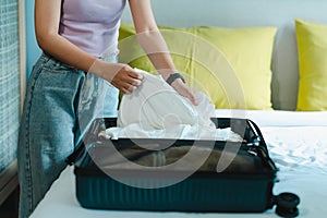 A teenage Asian woman folds up her shirt and pants in a suitcase on her bed to prepare for a weekend trip. Pack your luggage and