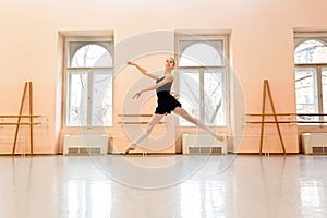 Teenage ballerina practicing ballet moves in large dancing studio