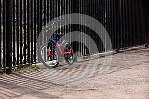 A teenage bike is tied to the fence of the schoolyard on a sunny day in spring and summer.