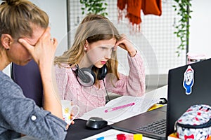 Teenage, blond girl in pink sweater is confused and asking her mother for help while doing her lessons. Her mother is drinking